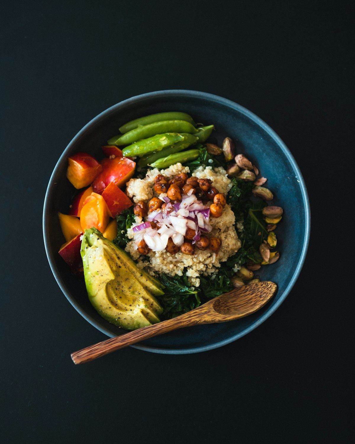 Ciotola con quinoa, ceci speziati, cavolo nero, avocado e pistacchi per un pasto vegano equilibrato